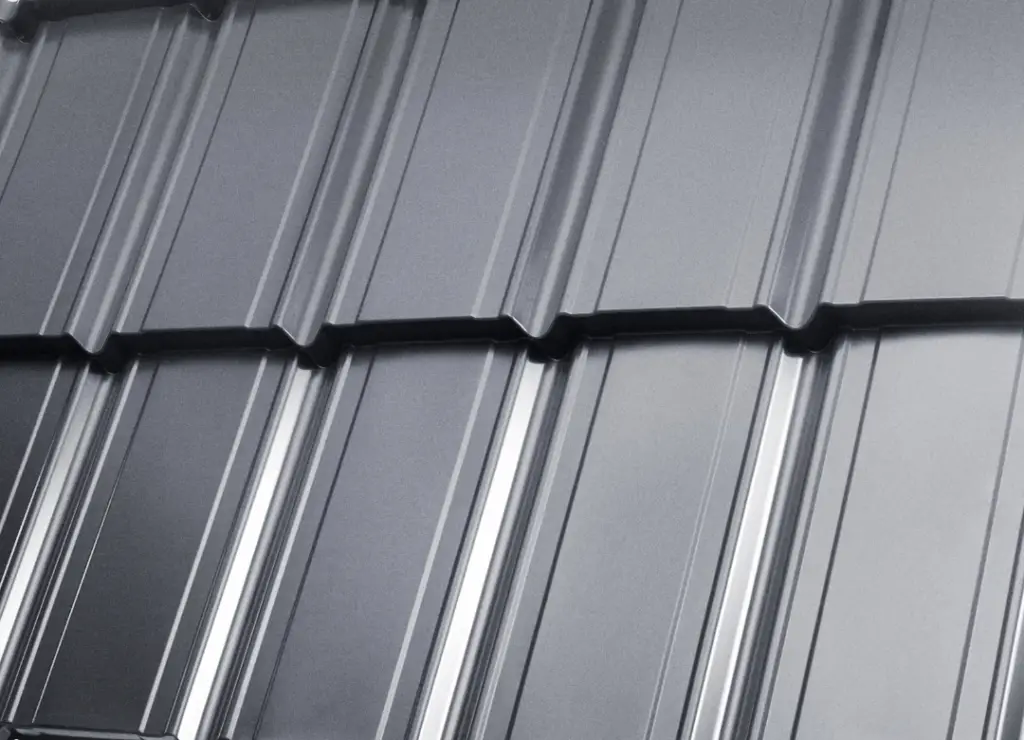 Close-up of a grey metal sheet with a corrugated design. The sheet features a series of parallel ridges and grooves, creating a textured surface. The material has a shiny finish, reflecting light across its smooth surface. Dominion Roofing | BRAMPTON | BURLINGTON | ETOBICOKE | MARKHAM | MISSISSAUGA | NORTH YORK | OAKVILLE | RICHMOND HILL | Scarborough | TORONTO | VAUGHAN | dominionroofing.com | Phone Number: 416-789-0601