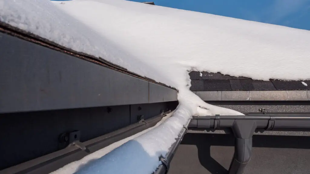 Snow accumulates on a slanted roof, partially melting into a drainpipe. As you enjoy the clear blue sky contrasting with the white snow and dark roofing material, remember to prepare your roof for winter to ensure it withstands the elements gracefully. Dominion Roofing | BRAMPTON | BURLINGTON | ETOBICOKE | MARKHAM | MISSISSAUGA | NORTH YORK | OAKVILLE | RICHMOND HILL | Scarborough | TORONTO | VAUGHAN | dominionroofing.com | Phone Number: 416-789-0601
