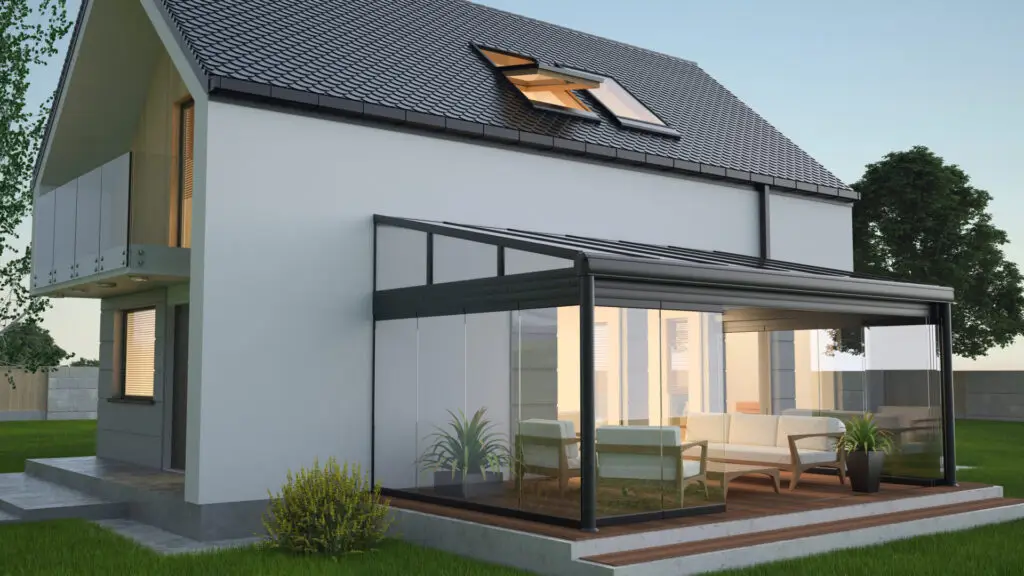 A modern house with a glass sunroom extension featuring lounge chairs and potted plants. The two-story building has a sloped roof and several windows. The setting includes a small lawn and a tree, under a clear sky. Dominion Roofing | BRAMPTON | BURLINGTON | ETOBICOKE | MARKHAM | MISSISSAUGA | NORTH YORK | OAKVILLE | RICHMOND HILL | Scarborough | TORONTO | VAUGHAN | dominionroofing.com | Phone Number: 416-789-0601