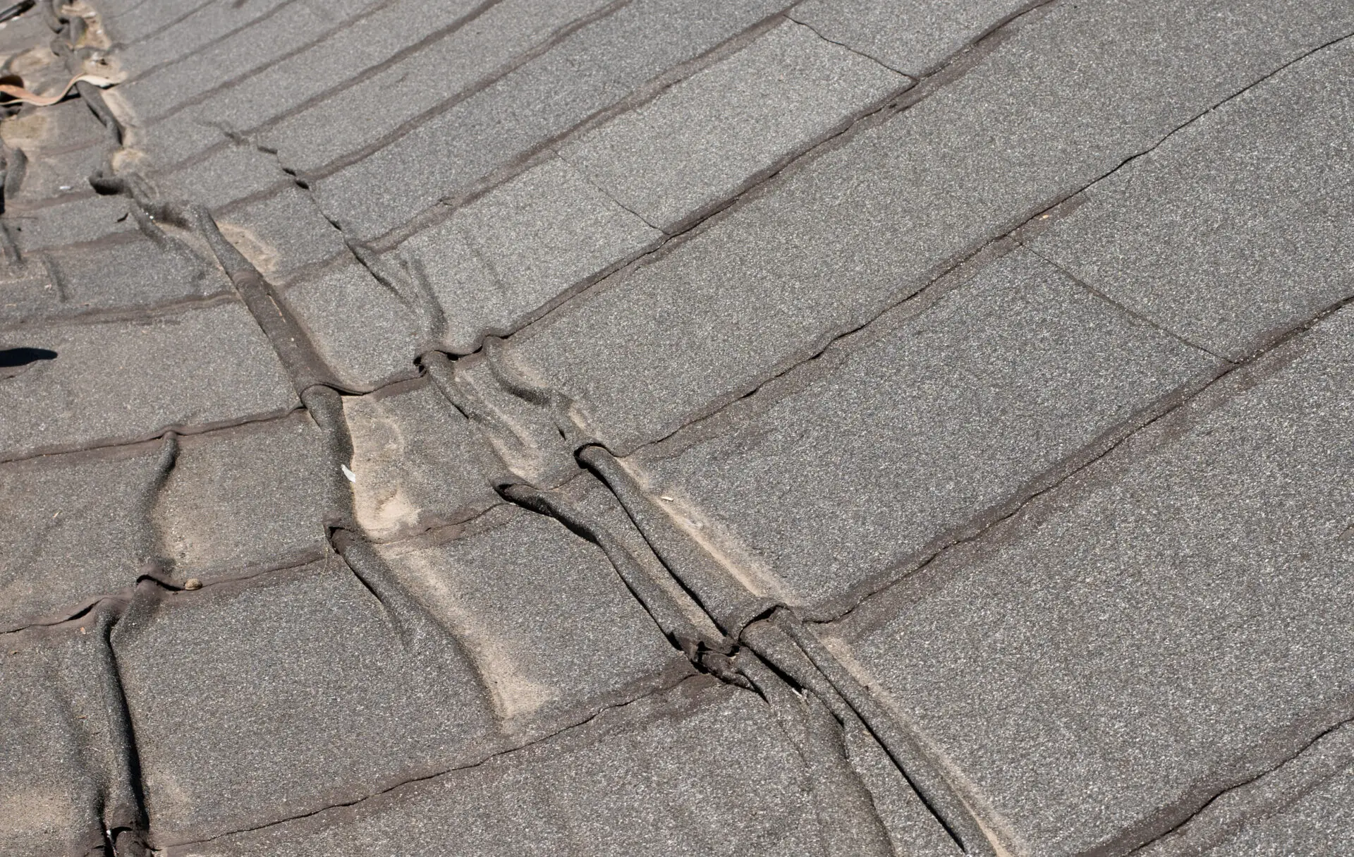 A close-up view of an asphalt shingle roof with visible wear and tear echoes the charm of aged residential flat roofing. The surface shows granule loss, discoloration, and uneven shingles, highlighting signs of age and potential need for repair or replacement. Dominion Roofing | BRAMPTON | BURLINGTON | ETOBICOKE | MARKHAM | MISSISSAUGA | NORTH YORK | OAKVILLE | RICHMOND HILL | Scarborough | TORONTO | VAUGHAN | dominionroofing.com | Phone Number: 416-789-0601