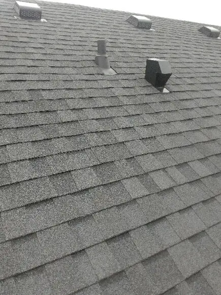 Gray shingled roof with several small vents and a chimney pipe, showcasing traditional residential shingle roofing. The shingles are uniformly arranged, covering the entire surface. The overcast sky casts a neutral lighting effect on the roof. Dominion Roofing | BRAMPTON | BURLINGTON | ETOBICOKE | MARKHAM | MISSISSAUGA | NORTH YORK | OAKVILLE | RICHMOND HILL | Scarborough | TORONTO | VAUGHAN | dominionroofing.com | Phone Number: 416-789-0601