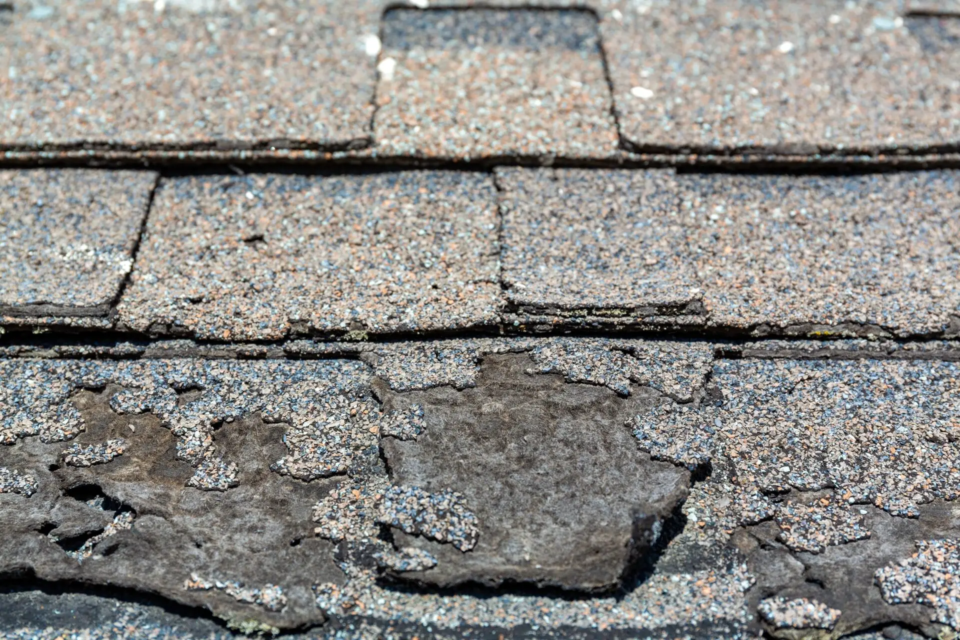 Close-up image of a worn asphalt shingle roof with noticeable granule loss and damage. The surface shows signs of aging, with patches where the underlying material is exposed, indicating a need for roof repair. Dominion Roofing | BRAMPTON | BURLINGTON | ETOBICOKE | MARKHAM | MISSISSAUGA | NORTH YORK | OAKVILLE | RICHMOND HILL | Scarborough | TORONTO | VAUGHAN | dominionroofing.com | Phone Number: 416-789-0601
