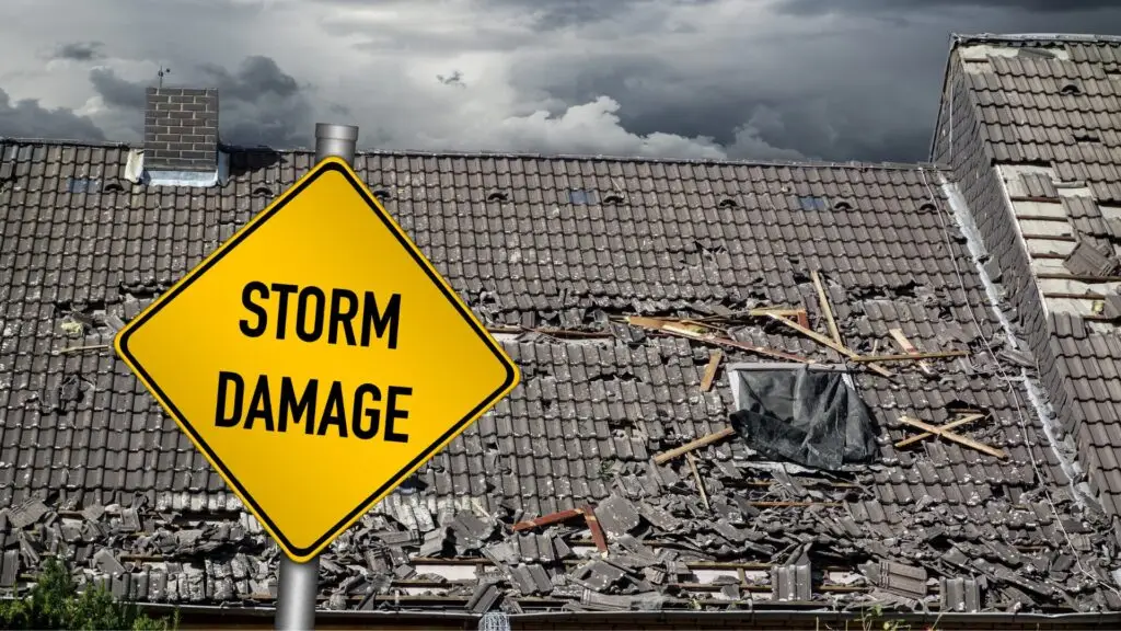 A damaged roof with missing and broken tiles is shown under a stormy, cloudy sky. In the foreground, a yellow diamond-shaped sign reads STORM DAMAGE, highlighting the destruction. Dominion Roofing | BRAMPTON | BURLINGTON | ETOBICOKE | MARKHAM | MISSISSAUGA | NORTH YORK | OAKVILLE | RICHMOND HILL | Scarborough | TORONTO | VAUGHAN | dominionroofing.com | Phone Number: 416-789-0601