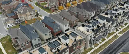 Aerial view of a suburban neighborhood with rows of modern, multi-story houses featuring various roofing styles. The streets and small yards are visible, with some autumn-colored trees scattered throughout the area. Dominion Roofing | BRAMPTON | BURLINGTON | ETOBICOKE | MARKHAM | MISSISSAUGA | NORTH YORK | OAKVILLE | RICHMOND HILL | Scarborough | TORONTO | VAUGHAN | dominionroofing.com | Phone Number: 416-789-0601