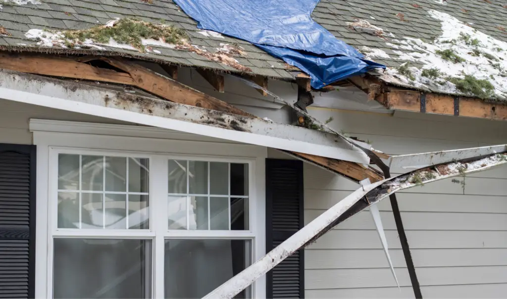 House with roof damage showing exposed wood and missing shingles, partially covered by a blue tarp. Snow is visible on the roof. A bent and broken gutter hangs down in front of a window with white shutters. Debris is scattered on the roof. Dominion Roofing | BRAMPTON | BURLINGTON | ETOBICOKE | MARKHAM | MISSISSAUGA | NORTH YORK | OAKVILLE | RICHMOND HILL | Scarborough | TORONTO | VAUGHAN | dominionroofing.com | Phone Number: 416-789-0601