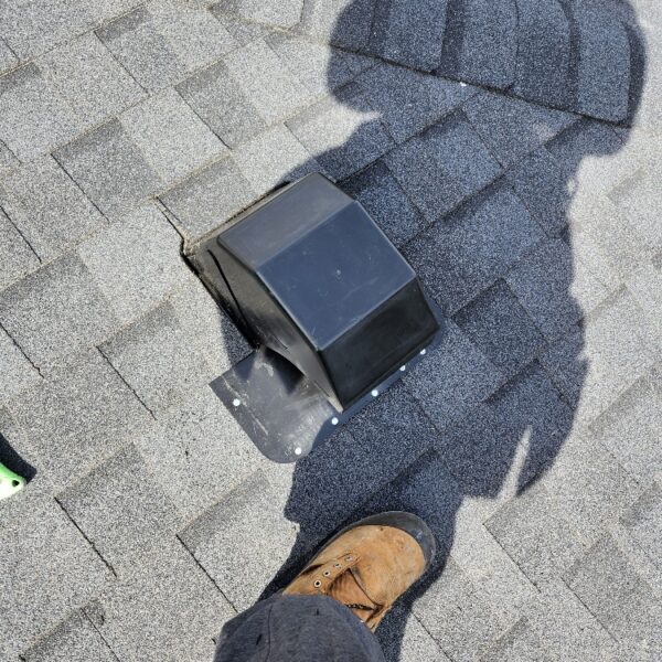 A person wearing a brown work boot stands on a gray shingled roof next to a black roof vent; the persons shadow is visible on the shingles. Dominion Roofing | BRAMPTON | BURLINGTON | ETOBICOKE | MARKHAM | MISSISSAUGA | NORTH YORK | OAKVILLE | RICHMOND HILL | Scarborough | TORONTO | VAUGHAN | dominionroofing.com | Phone Number: 416-789-0601