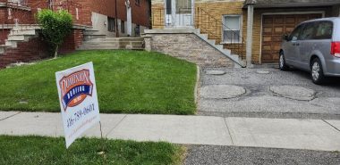 A house with a Canadian flag on the balcony, a car parked in the driveway, and a “Dominion Lending Centres” sign with a phone number on the lawn. The sky is overcast and there are trees and another house nearby. Dominion Roofing | BRAMPTON | BURLINGTON | ETOBICOKE | MARKHAM | MISSISSAUGA | NORTH YORK | OAKVILLE | RICHMOND HILL | Scarborough | TORONTO | VAUGHAN | dominionroofing.com | Phone Number: 416-789-0601