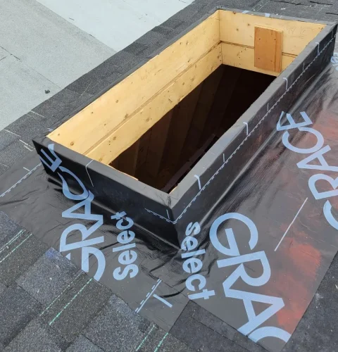 Rectangular skylight opening on a roof under construction. The roofing is covered with black waterproof membrane labeled GRACE Select. Surrounding shingles are gray. The wooden frame is visible inside the opening. Dominion Roofing | BRAMPTON | BURLINGTON | ETOBICOKE | MARKHAM | MISSISSAUGA | NORTH YORK | OAKVILLE | RICHMOND HILL | Scarborough | TORONTO | VAUGHAN | dominionroofing.com | Phone Number: 416-789-0601