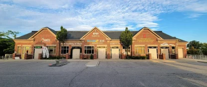 A single-story brick building hosts several businesses, including a music academy and a BBQ restaurant. With trees out front and a clear sky above, the facility showcases its fresh commercial shingle roofing. The parking lot is mostly empty, with a small stack of materials on the ground. Dominion Roofing | BRAMPTON | BURLINGTON | ETOBICOKE | MARKHAM | MISSISSAUGA | NORTH YORK | OAKVILLE | RICHMOND HILL | Scarborough | TORONTO | VAUGHAN | dominionroofing.com | Phone Number: 416-789-0601